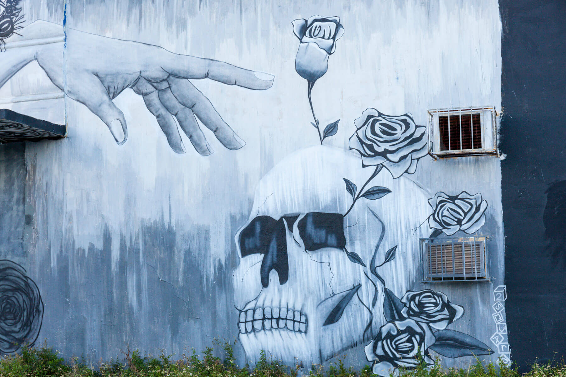 Graffiti mural of a hand reaching a skull with roses